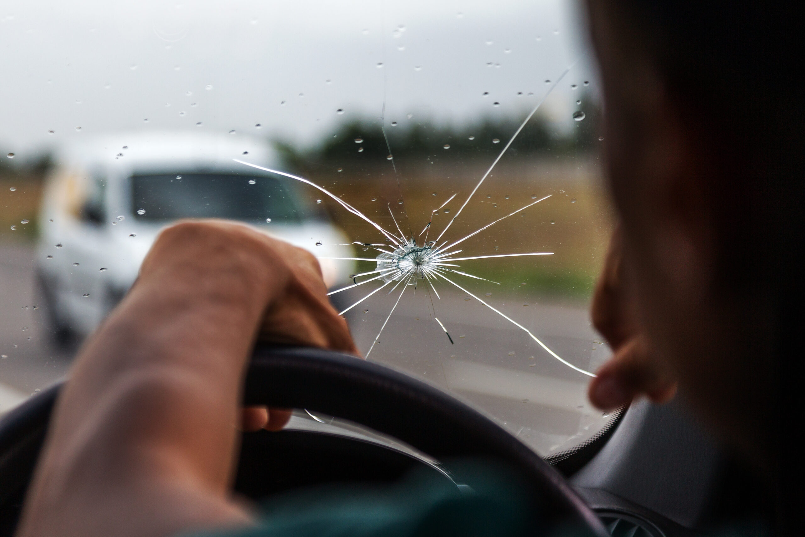 Broken windshield of a car. A web of radial splits, cracks on the triplex windshield. Broken car windshield, damaged glass with traces of oncoming stone on road or from bullet trace in car glass